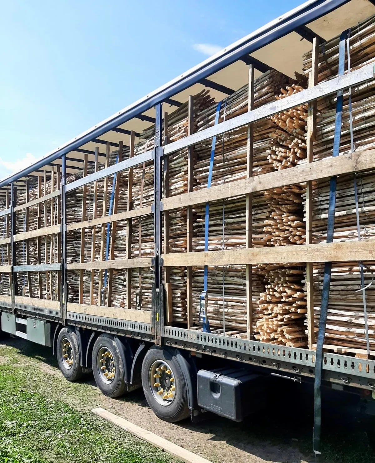 Een schuifzeiloplegger met opengeschoven zeil, tot het dak geladen met hekwerk van hazelaar tussen houten rongen, en vastgesjord.