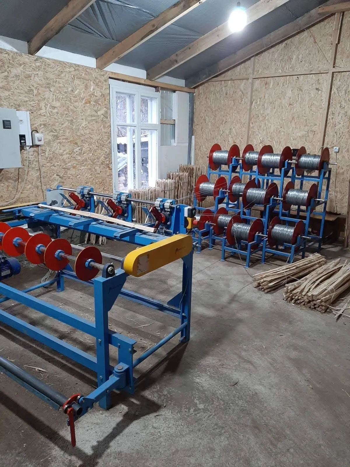 The fence roll machine in our workshop, with the reels of wire that feed it and bundles of split pickets on the floor.